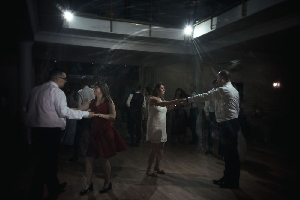 People dancing together in a dark moody room illuminated by overhead lights casting atmospheric shadows.