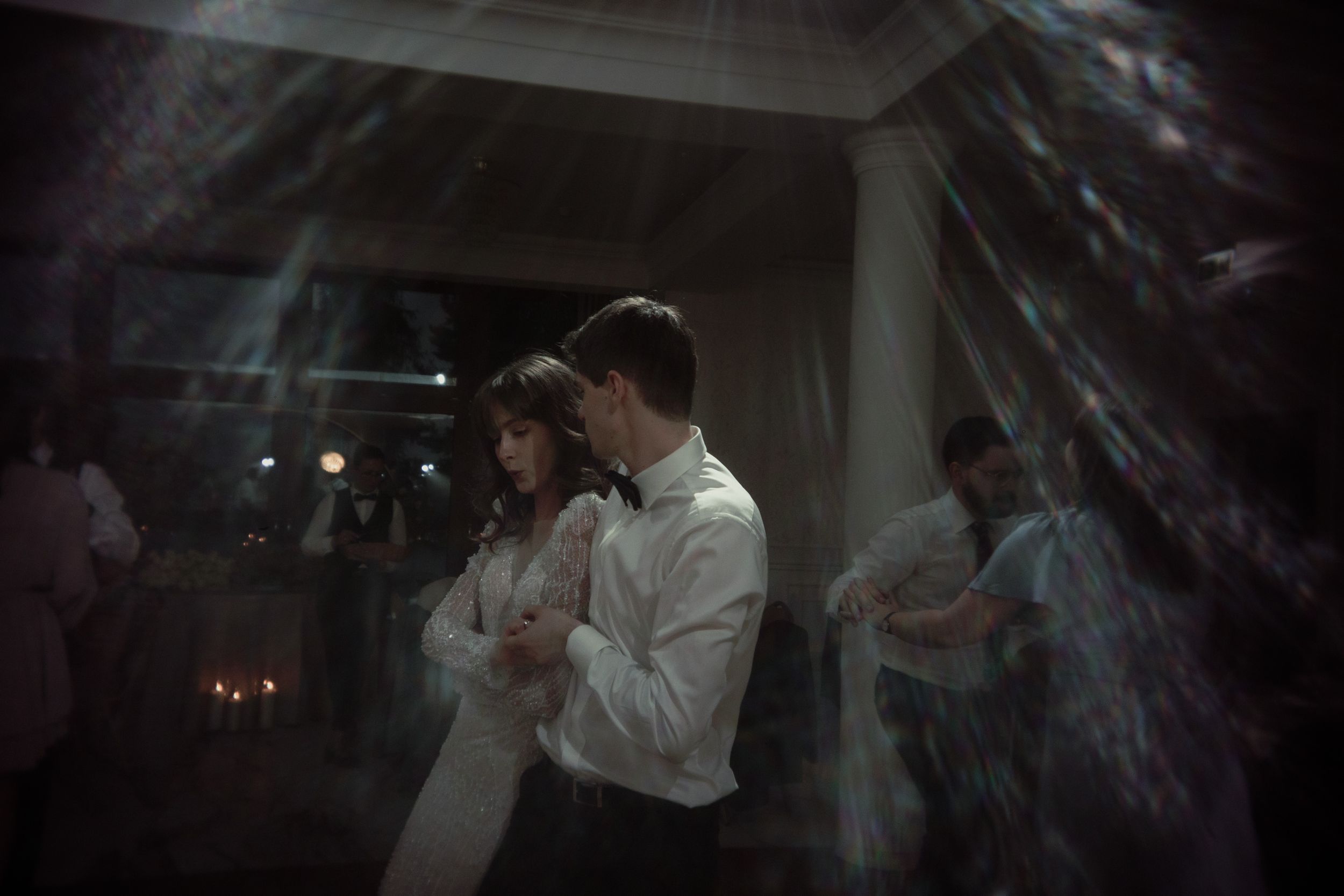 A couple slow dances in a dimly lit reception space with atmospheric lighting and decorative elements.