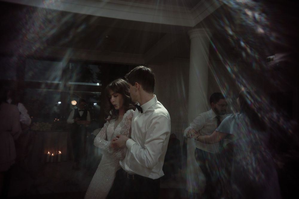 A couple slow dances in a dimly lit reception space with atmospheric lighting and decorative elements.
