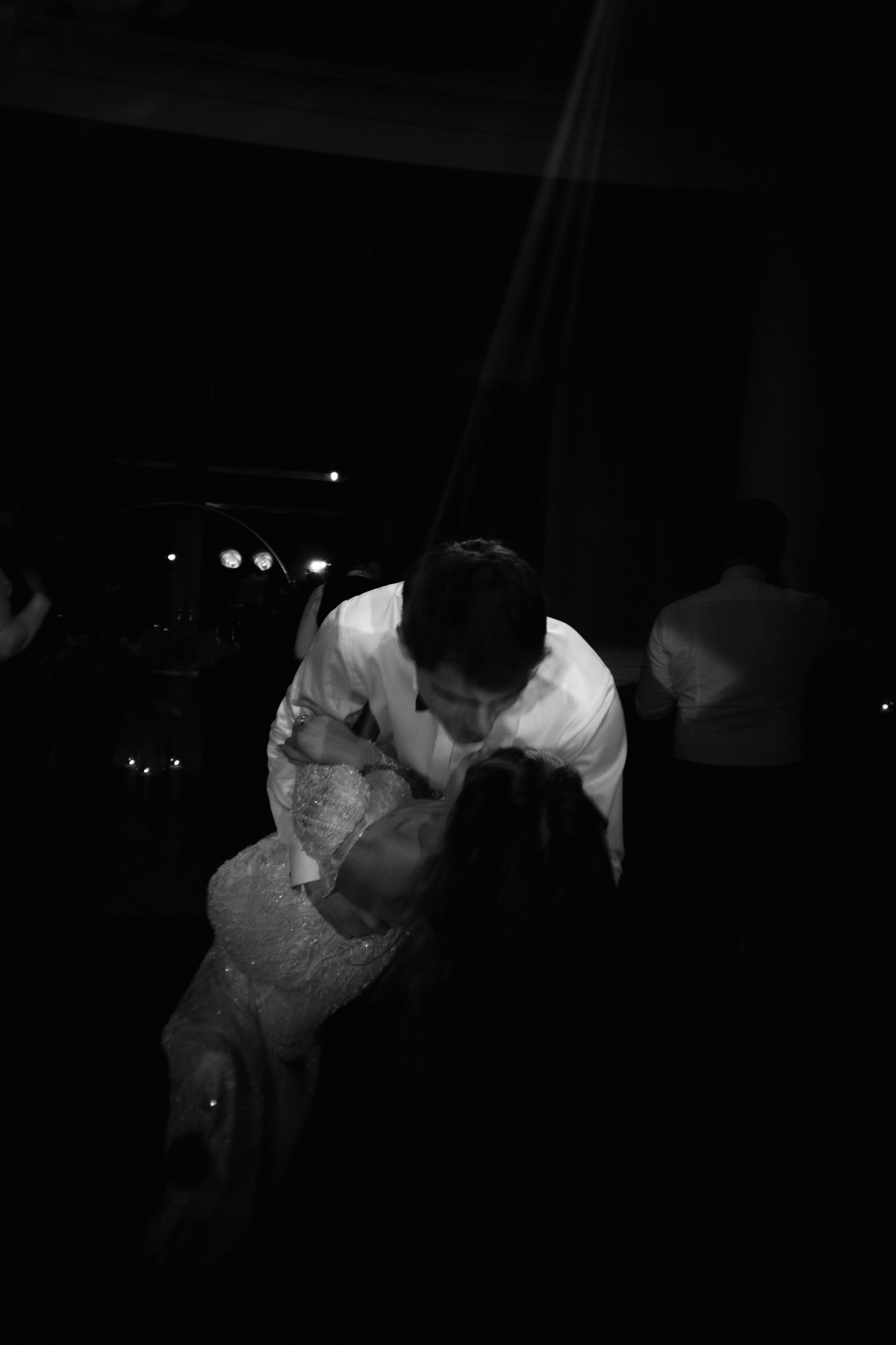 A couple embraces during a slow dance in black and white lighting at an evening event.
