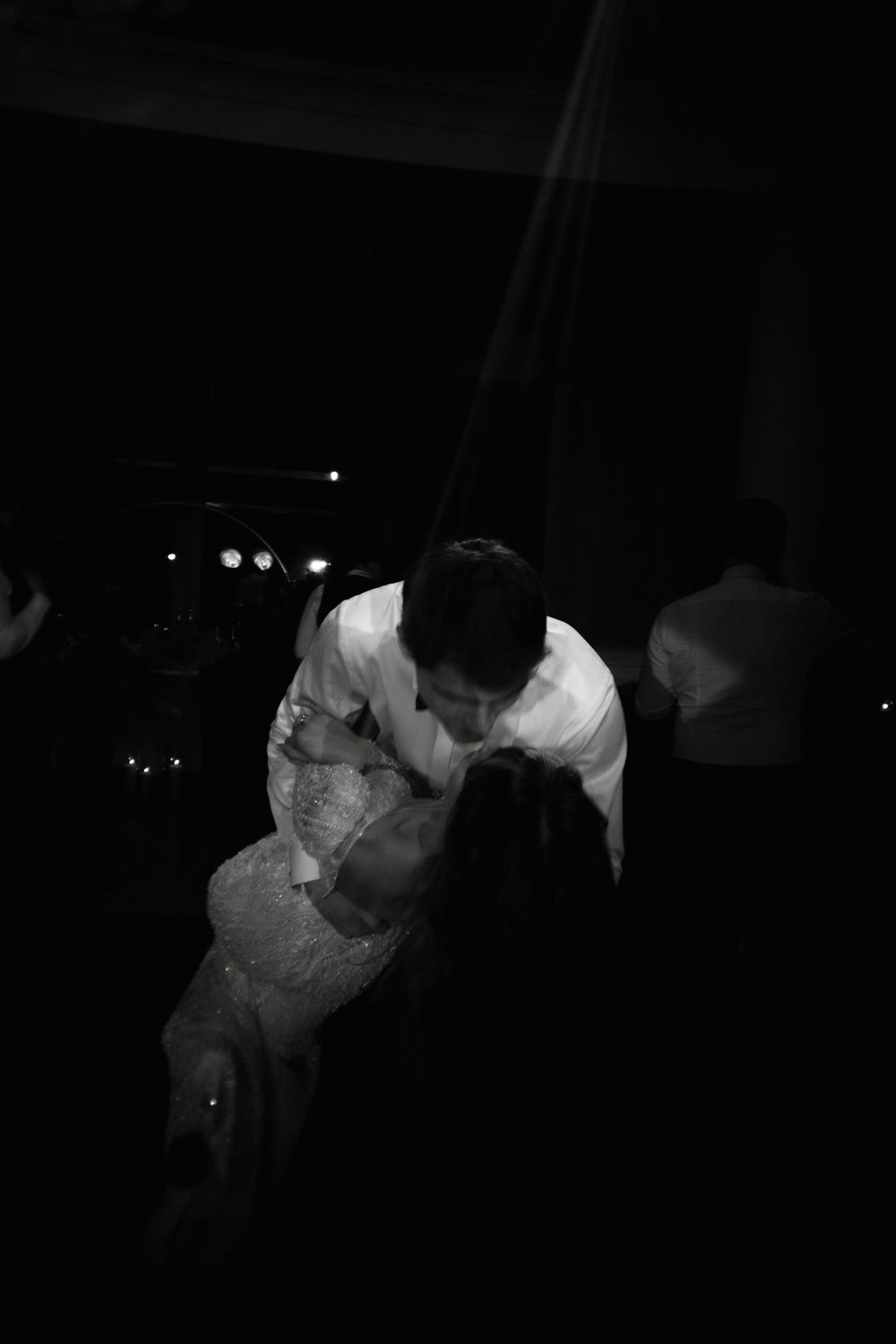 A couple embraces during a slow dance in black and white lighting at an evening event.