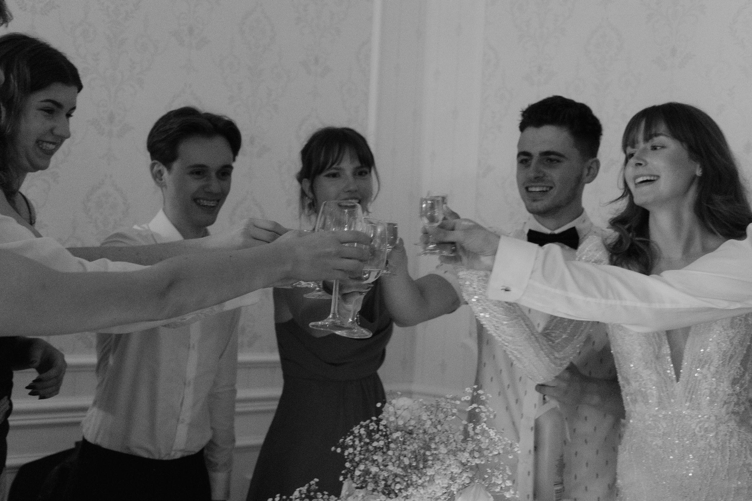 A group of people in formal attire raise their glasses in a celebratory toast at what appears to be a wedding reception.
