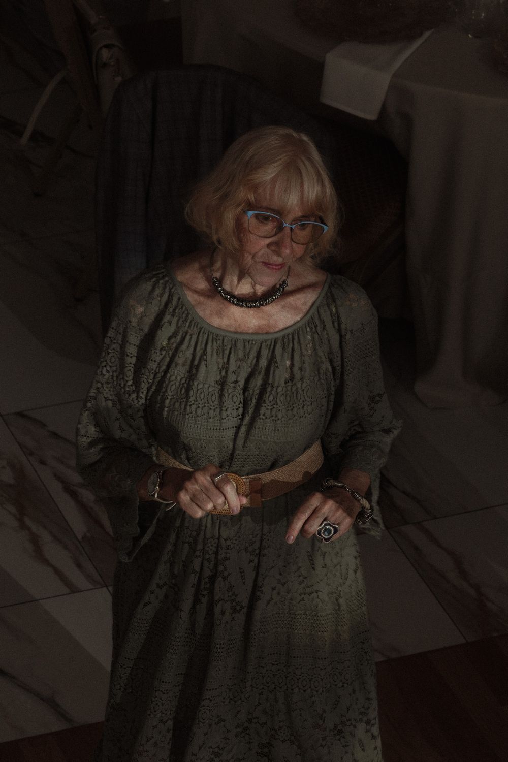 Person in glasses wearing an olive green dress writes in a dimly lit room.