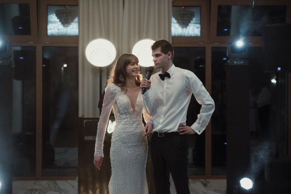 Couple in formal wear dancing together at an elegant venue with round paper lanterns and window backdrop at night.