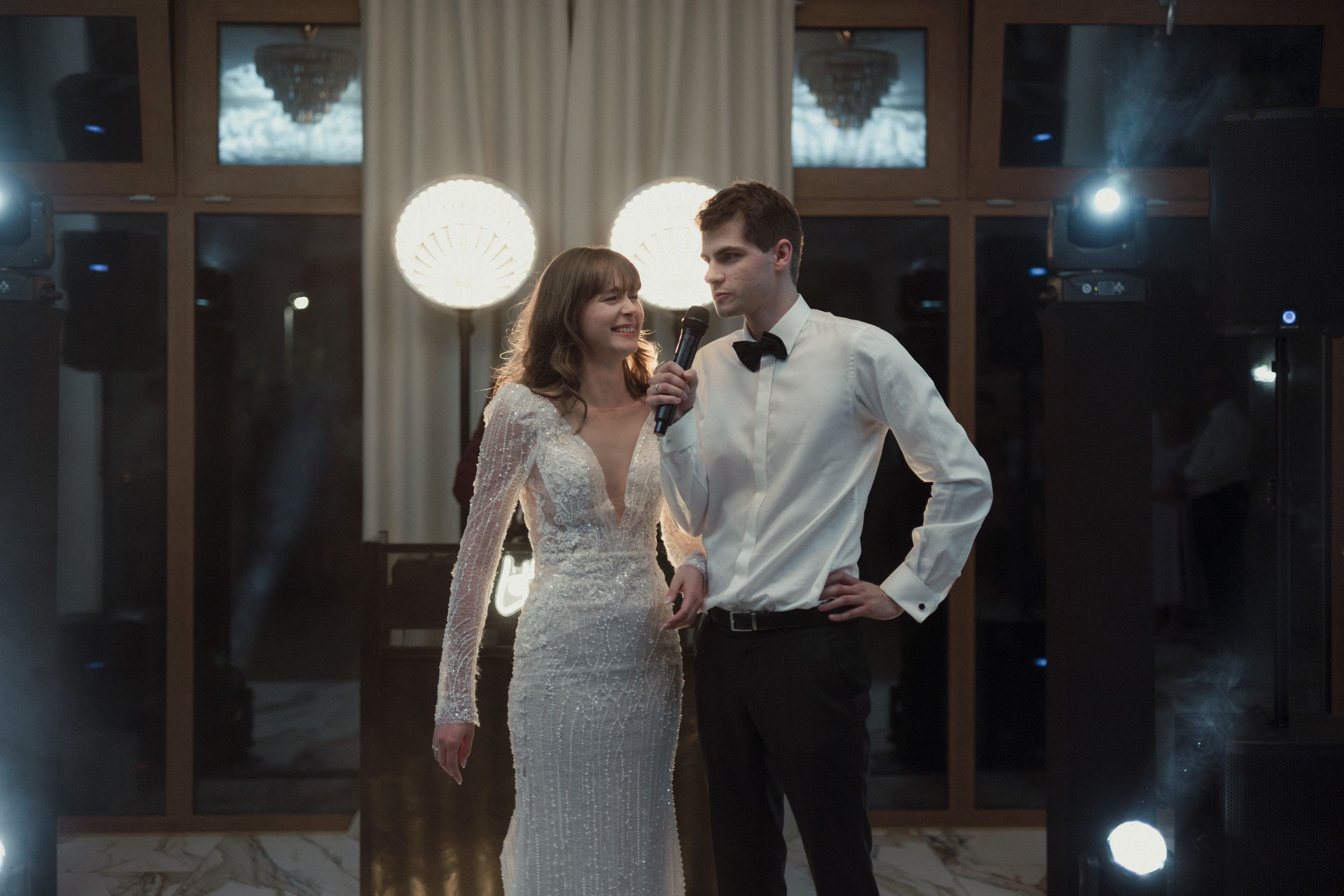 Couple in formal wear dancing together at an elegant venue with round paper lanterns and window backdrop at night.