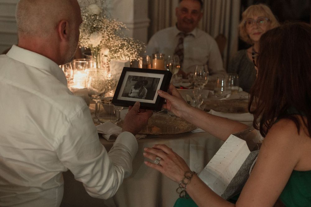People looking at a digital photo frame during a dinner party with chandeliers in the background.