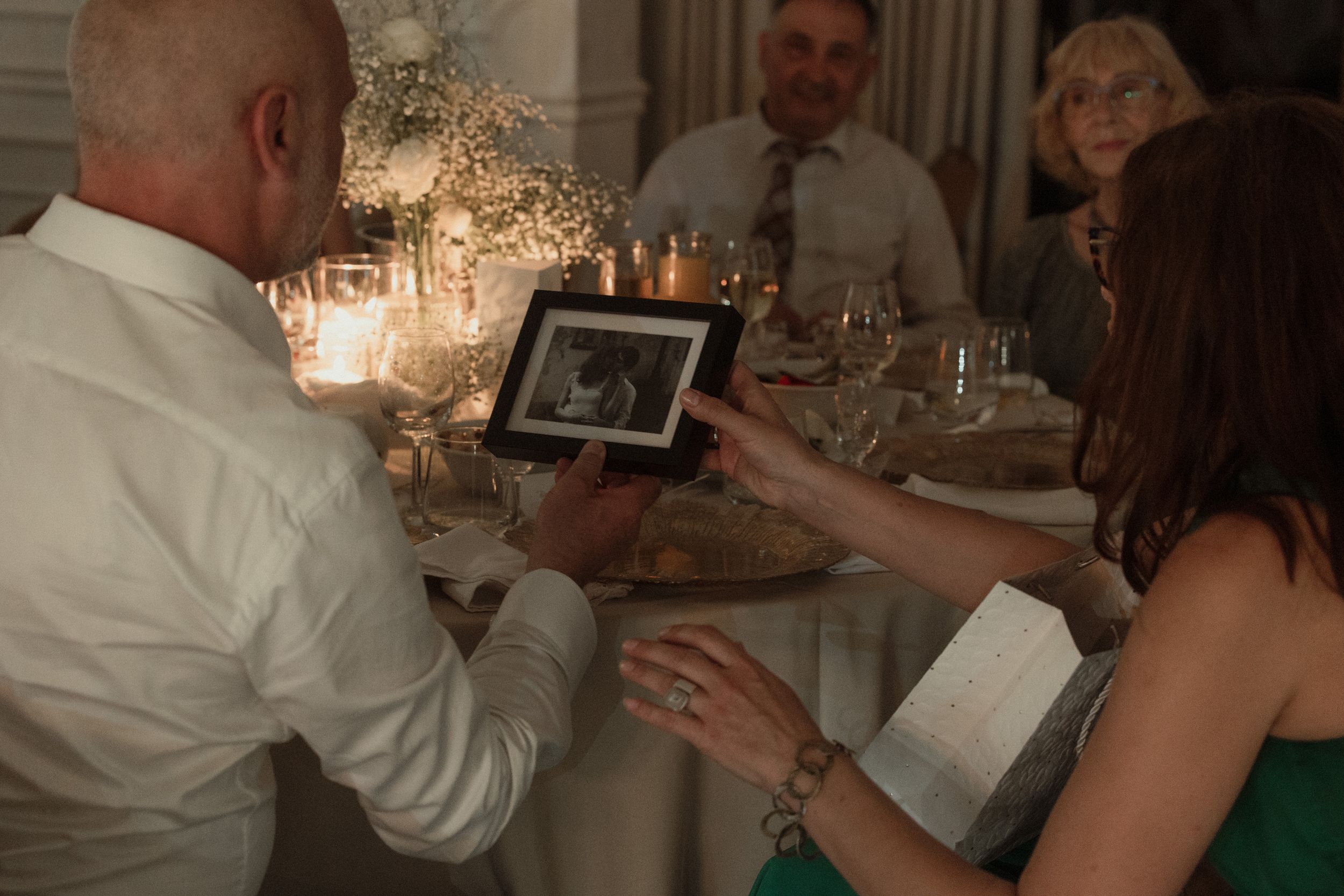 People looking at a digital photo frame during a dinner party with chandeliers in the background.
