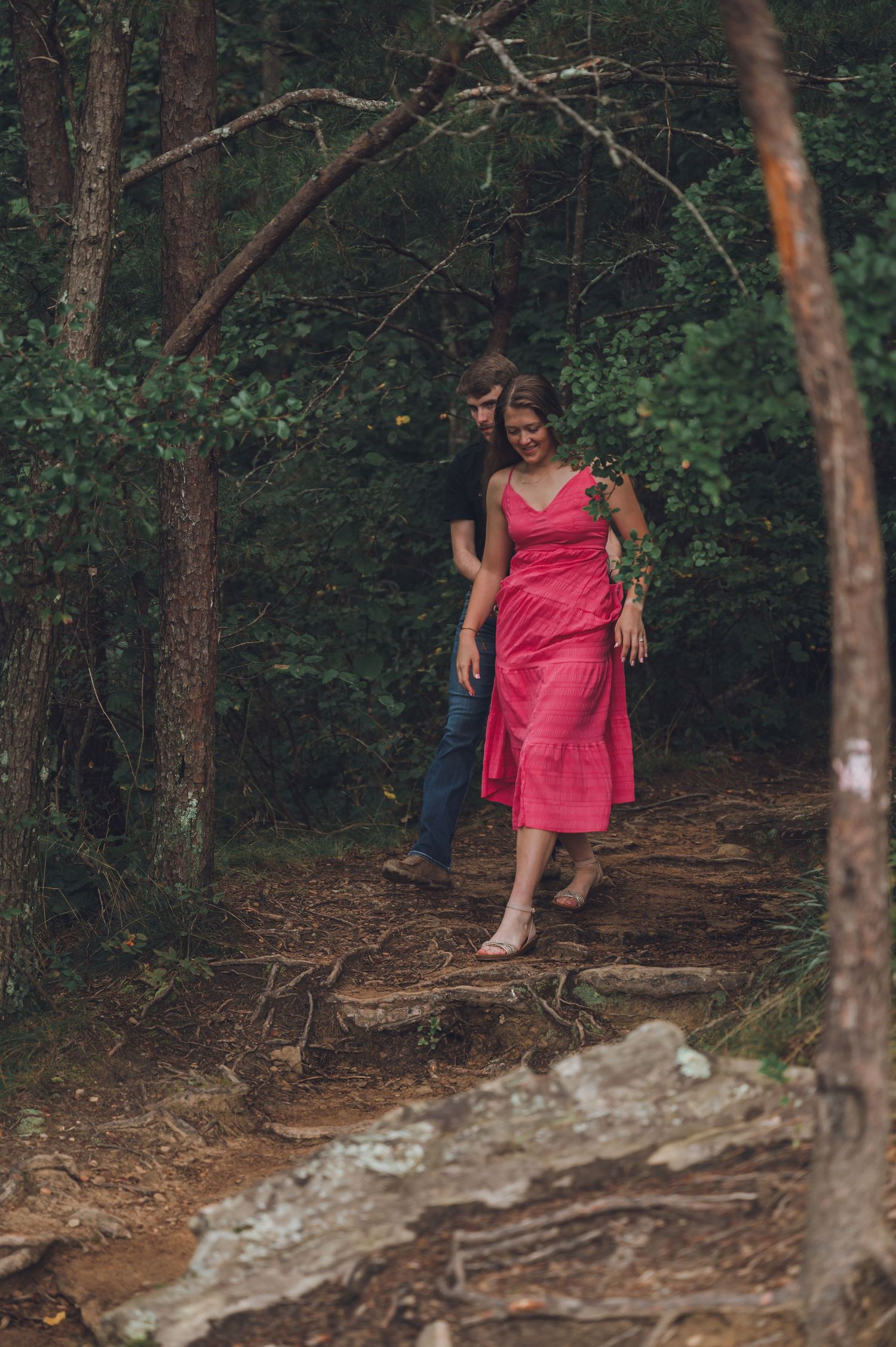 A person wearing a bright red dress walks along a wooded forest trail on a summer day.