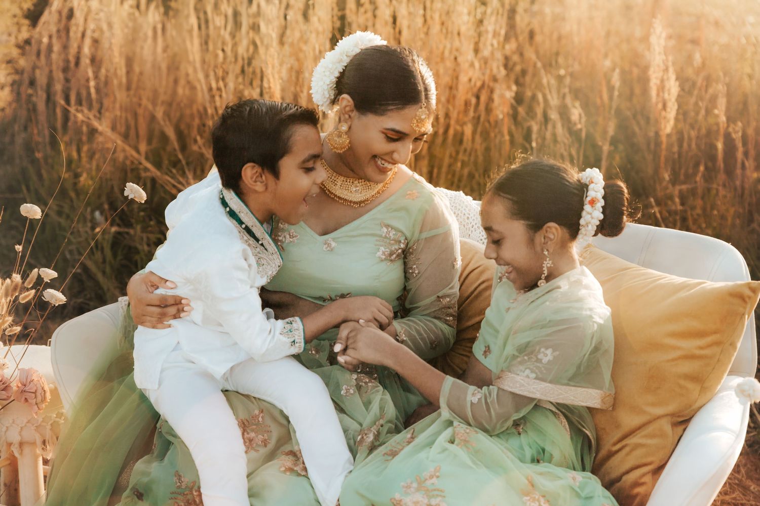 A tender family bonding moment captured at golden hour in a field with tall grass and warm lighting.