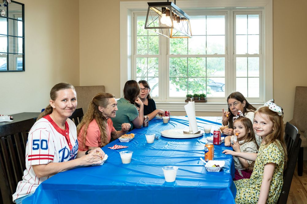 Group of people seated at a long table with blue tablecloths in a bright room.