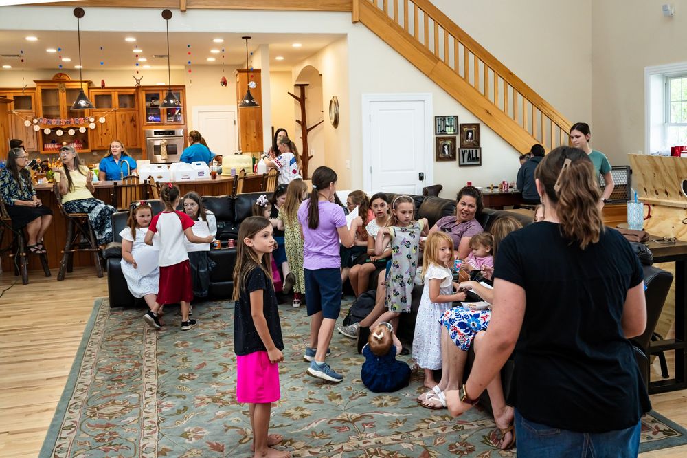 Wide view of a party room with people gathered around tables and chairs.