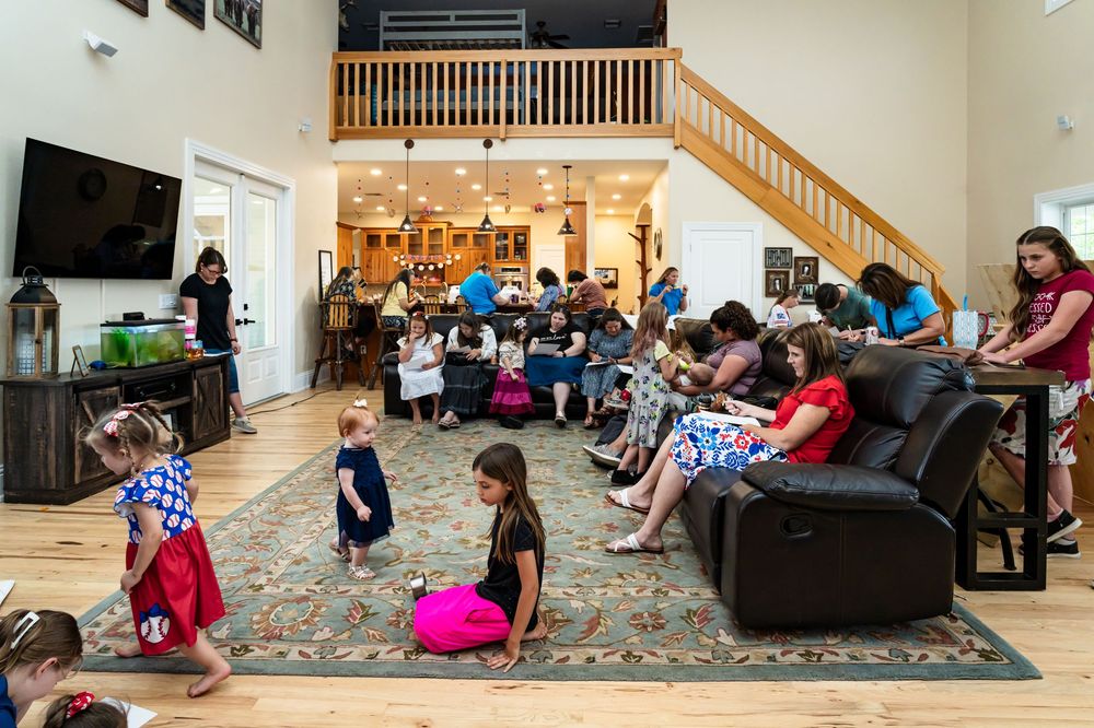 Large room with wooden staircase and people seated on floor and furniture.