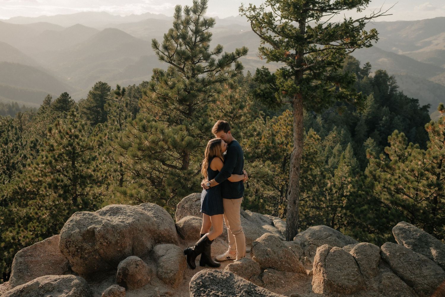 Couple admiring a scenic mountain vista from a rocky overlook during sunset in Colorado.