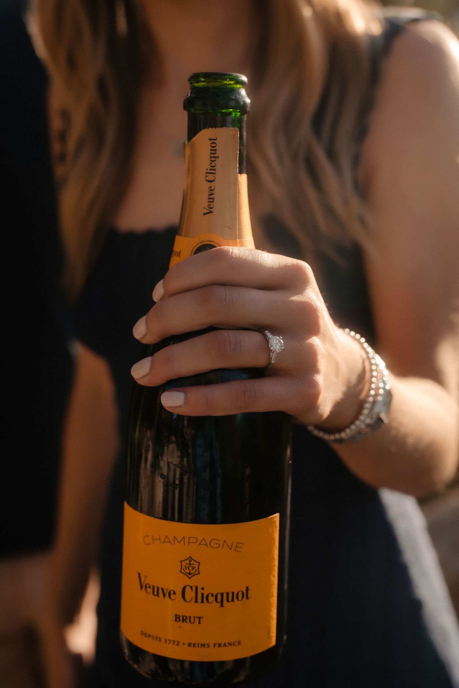 Hands holding a bottle of Veuve Clicquot champagne in an atmospheric dark setting with soft lighting.