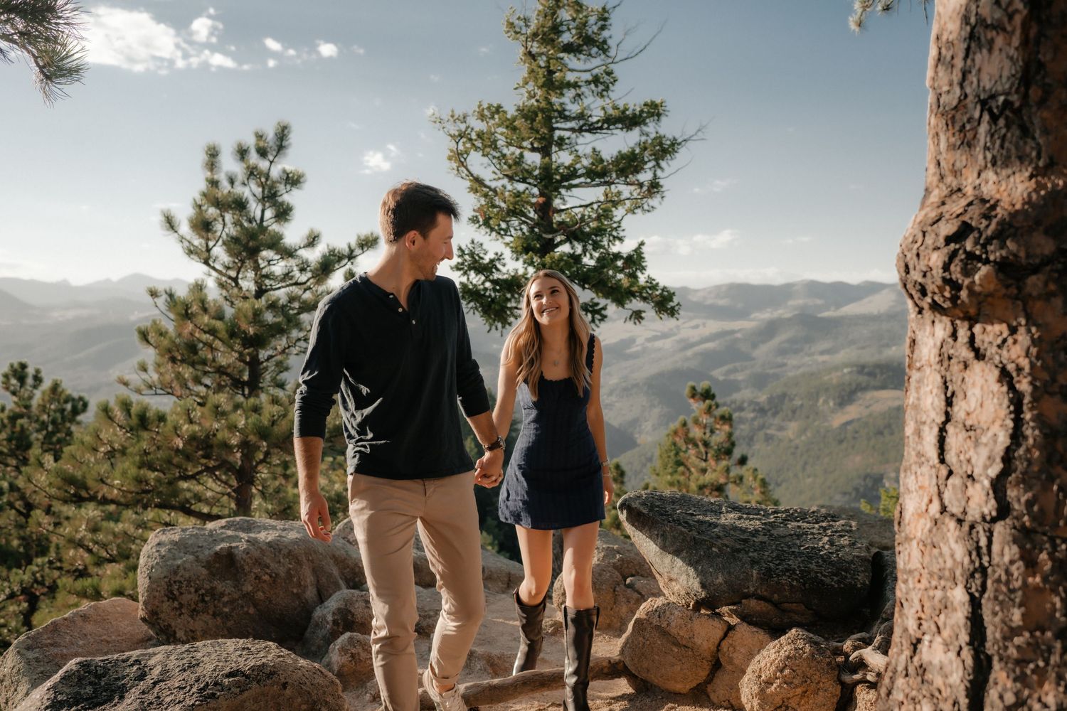 A couple enjoying a scenic mountain hike together among pine trees and rocks with panoramic valley views.