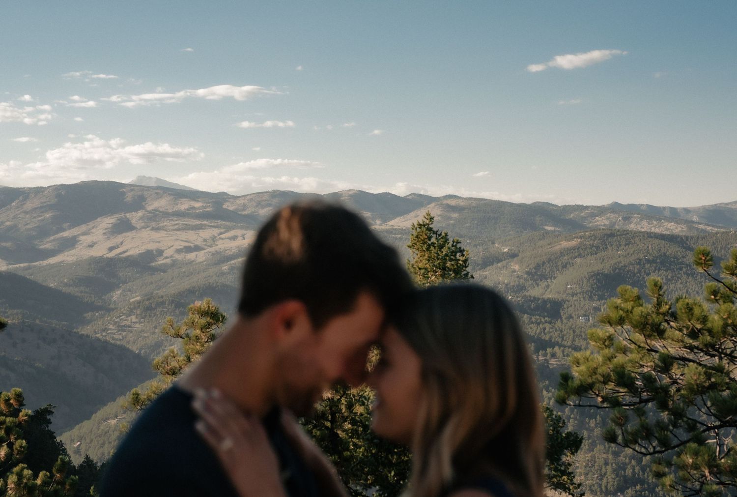 A romantic silhouette against a backdrop of rolling mountains and blue skies in a scenic outdoor setting.