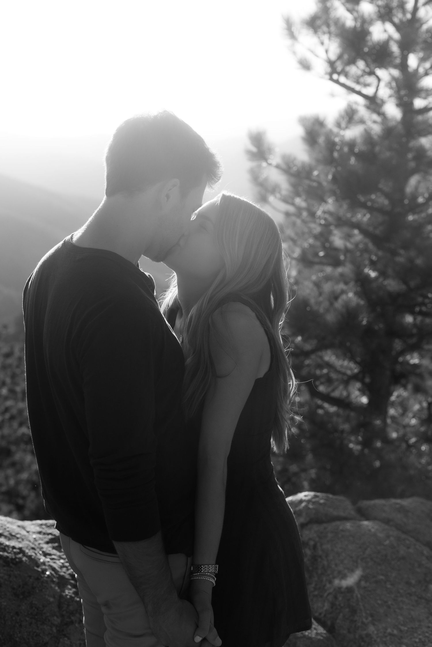 A romantic black and white photo series shows a couple in silhouette standing close together on a hillside with trees.