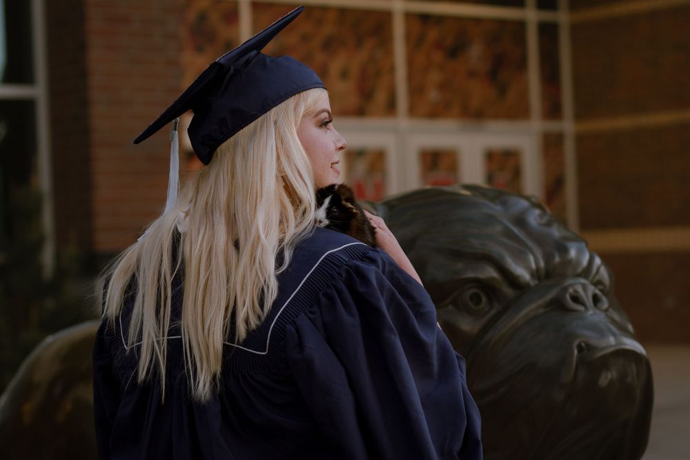Spokane college graduate holding hamster over shoulder while smiling for pet and grad portrait session.