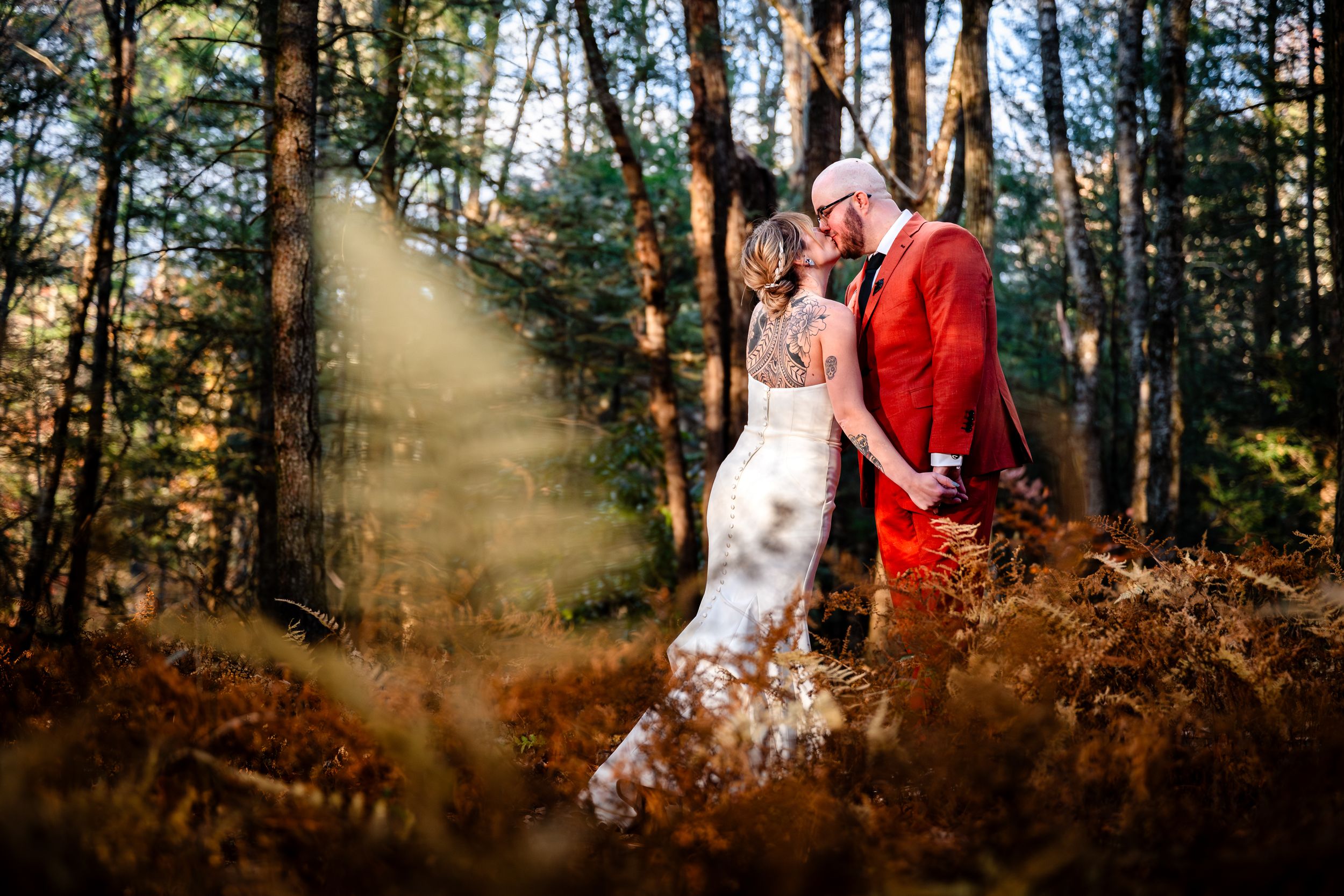 Sunlit wedding photos captured through pine trees creating magical forest atmosphere.
