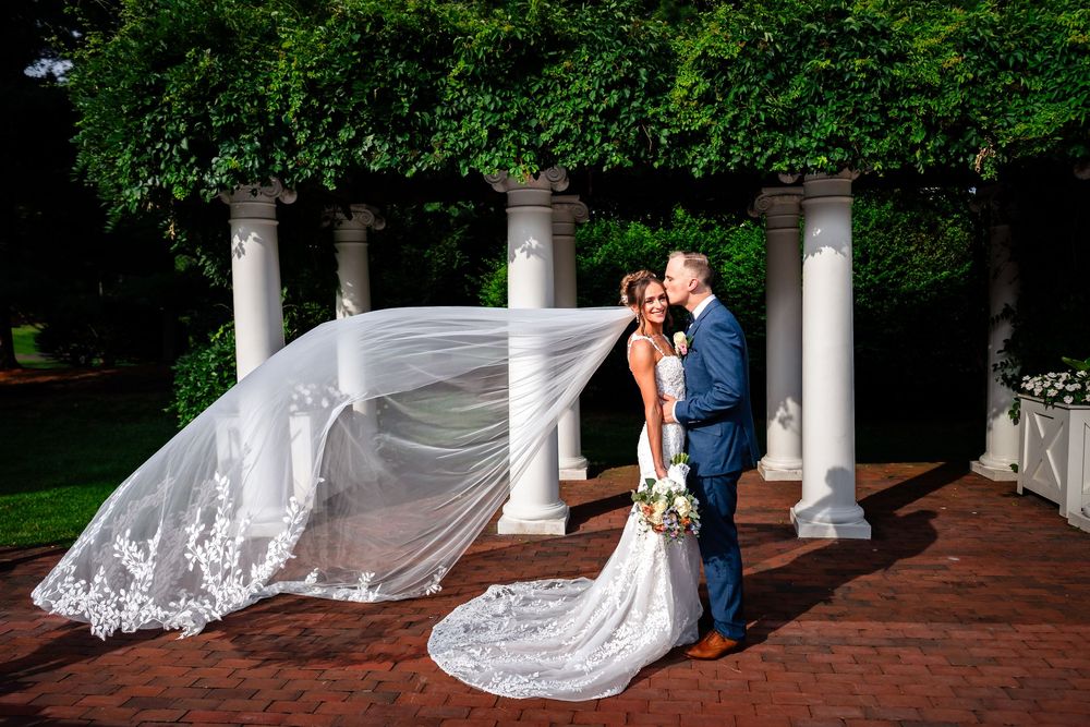 Bride's veil flows dramatically in the wind during outdoor wedding photo session.