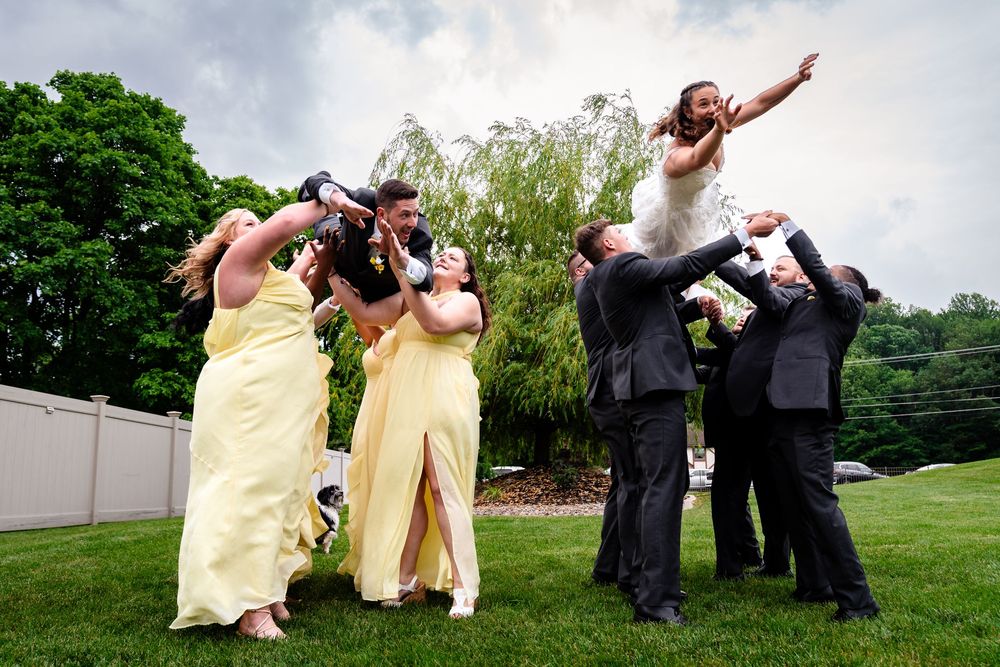 Wedding party in yellow dresses poses playfully on grassy hillside.