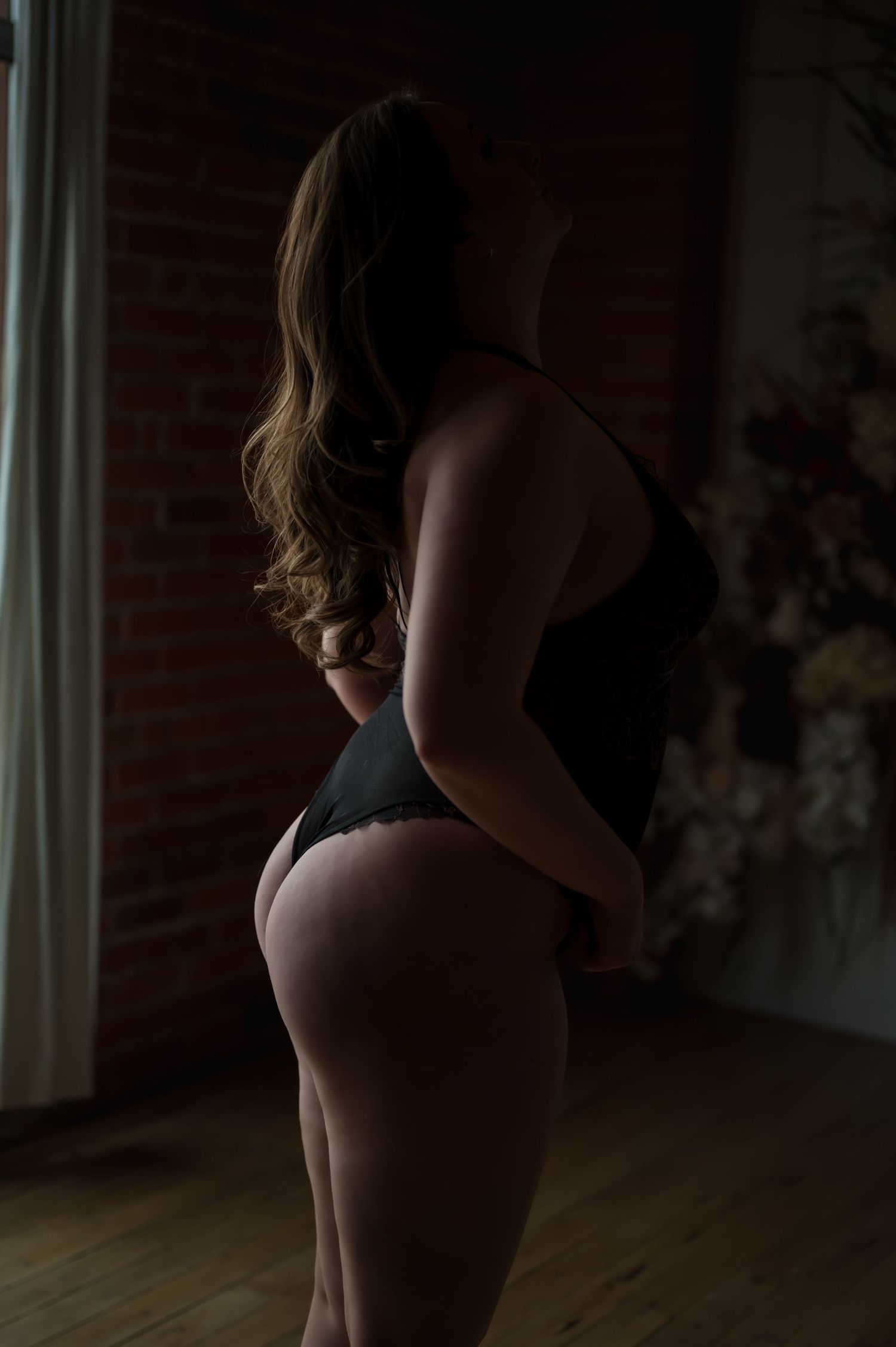 Modern boudoir photography with natural window light and exposed brick wall.