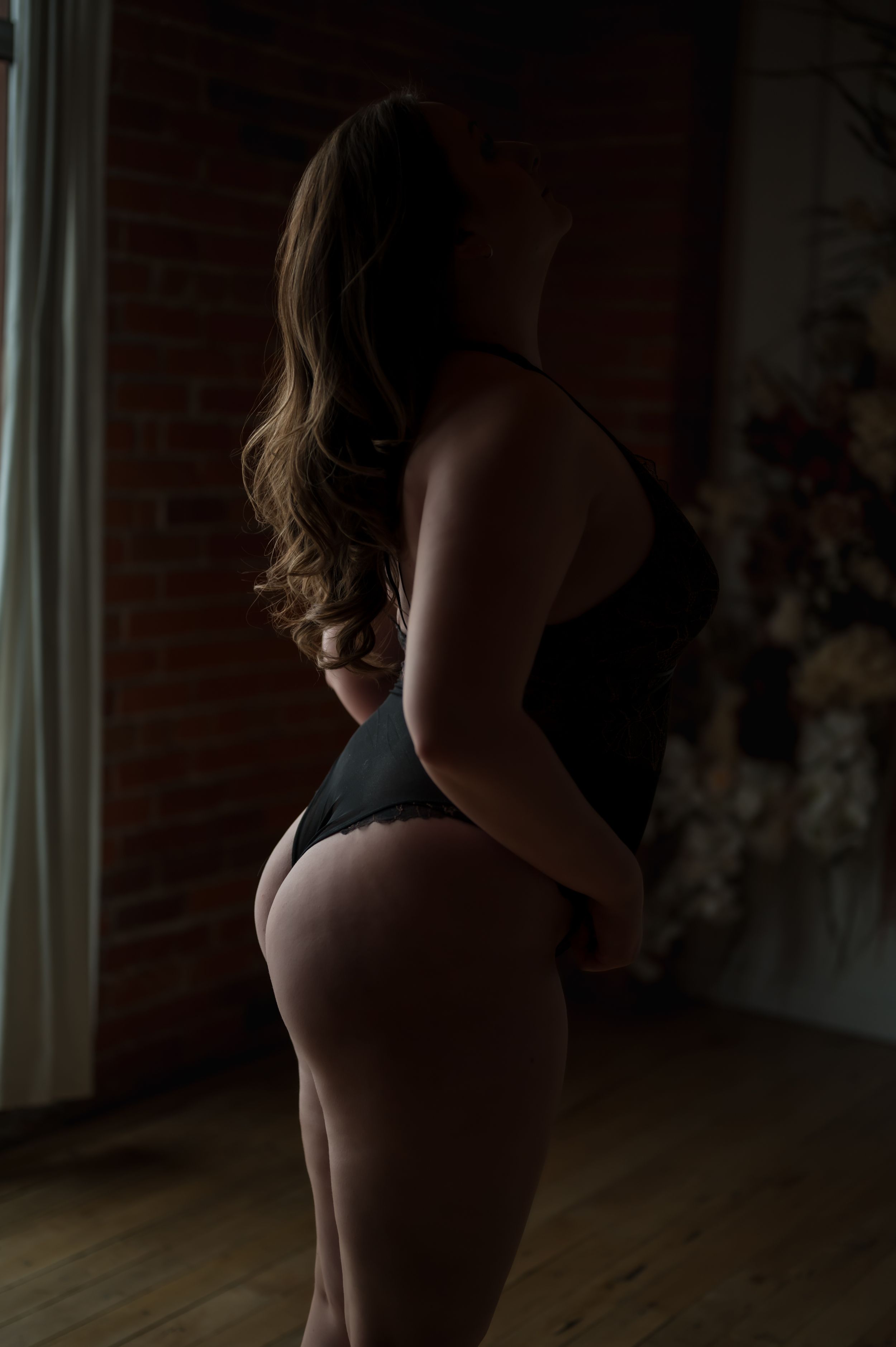 Modern boudoir photography with natural window light and exposed brick wall.