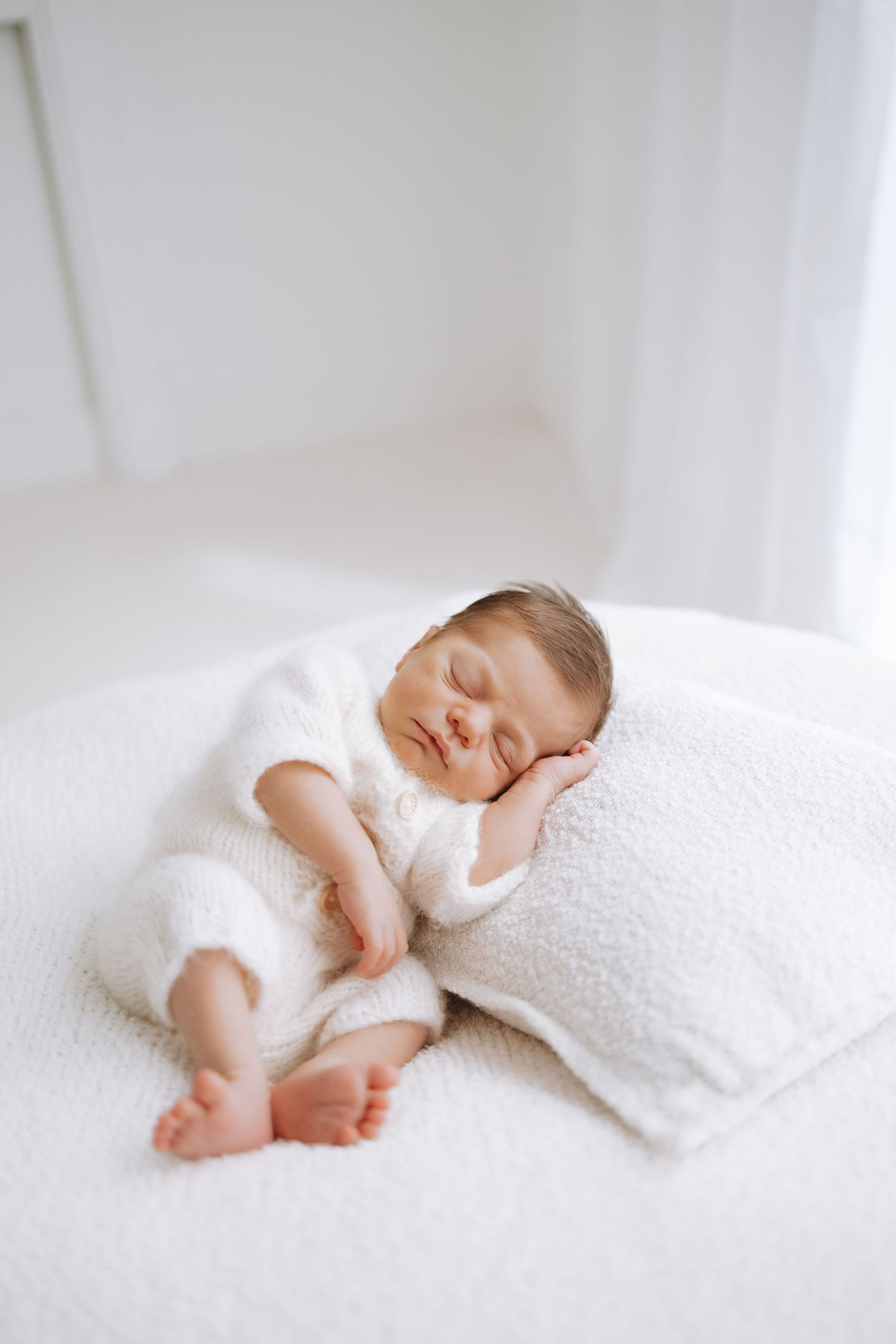 A peaceful sleeping baby swaddled in white lying on soft white bedding with feet peeking out.