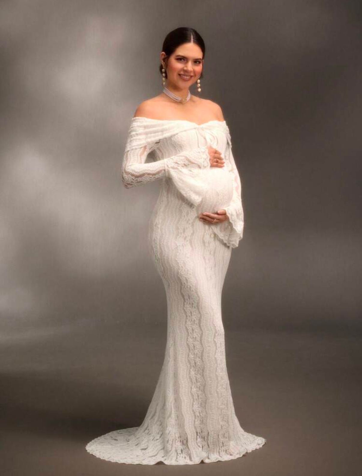 An off-shoulder white lace gown creates romantic movement against a dark backdrop.