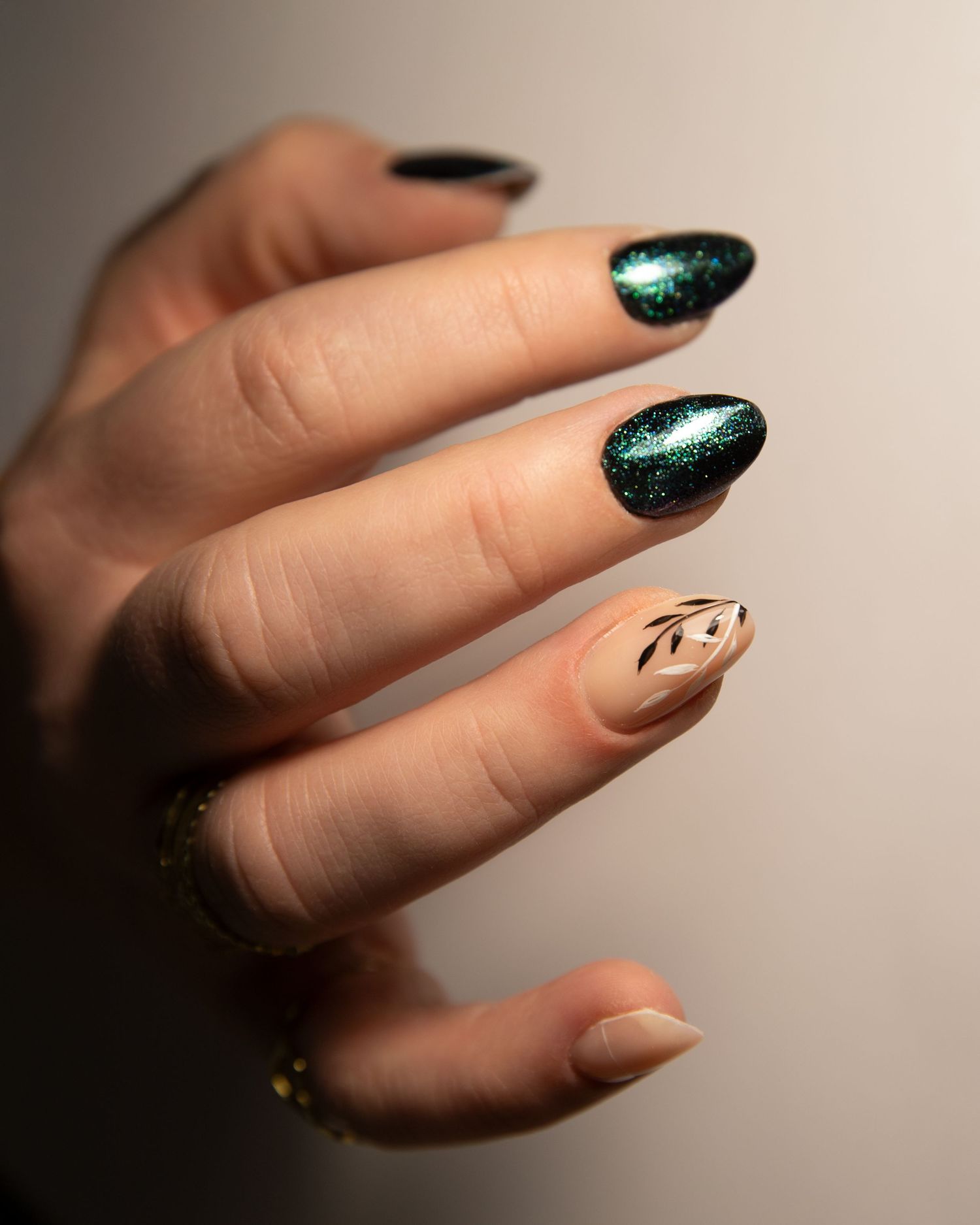 Elegant nail art close-up featuring sparkling dark green and nude tones with delicate line accents.