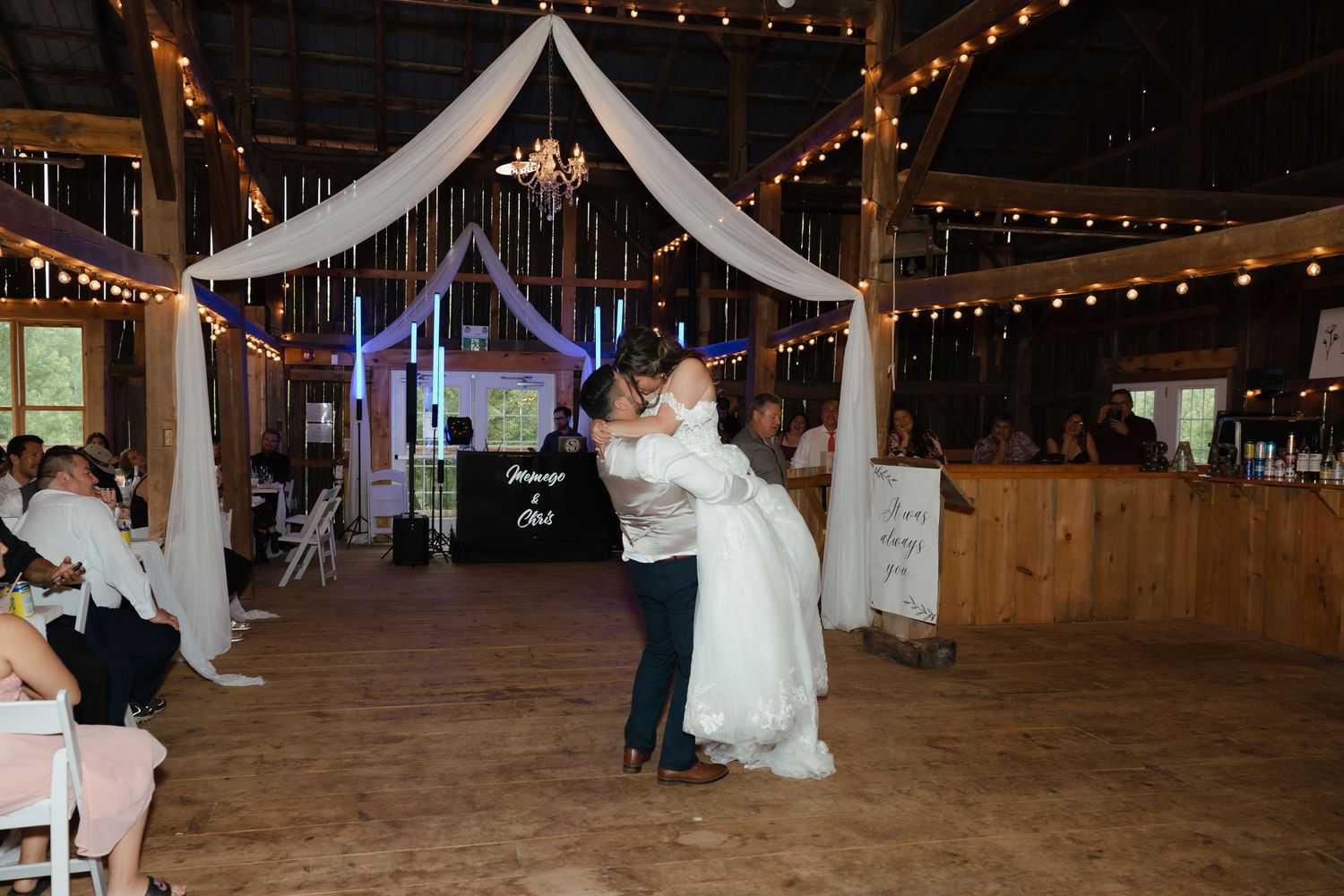 Wedding venue barn interior decorated with twinkle lights and white fabric draping creates romantic reception atmosphere.