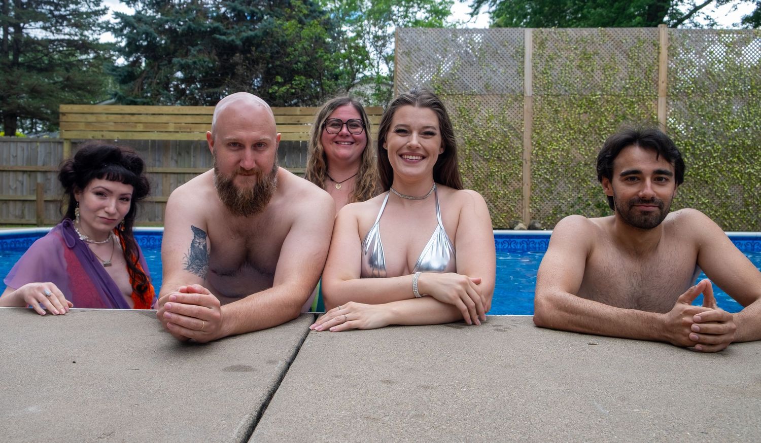 Groups of people relax and smile while sitting around an above-ground swimming pool on a sunny summer day.