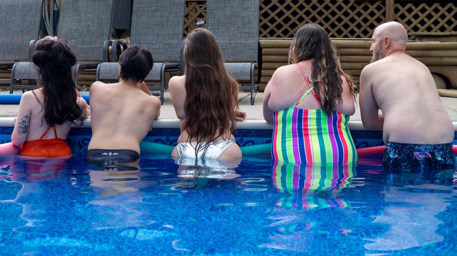 Poolside attendees facing away from camera watching a water performance in an aqua blue swimming pool.
