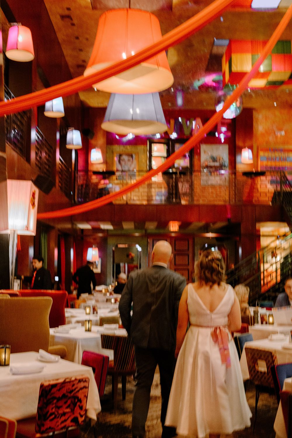 Upscale restaurant interior with red lighting, white tablecloths and pendant lamps creating an elegant dining atmosphere.