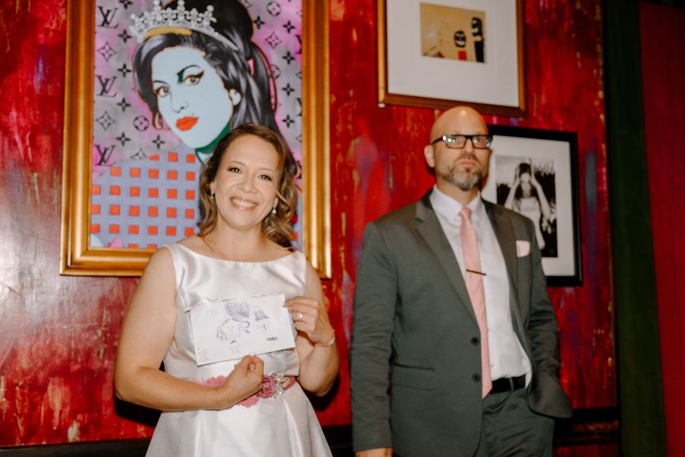 Wedding couple poses against red wall with pop art and framed artwork in stylish urban venue.