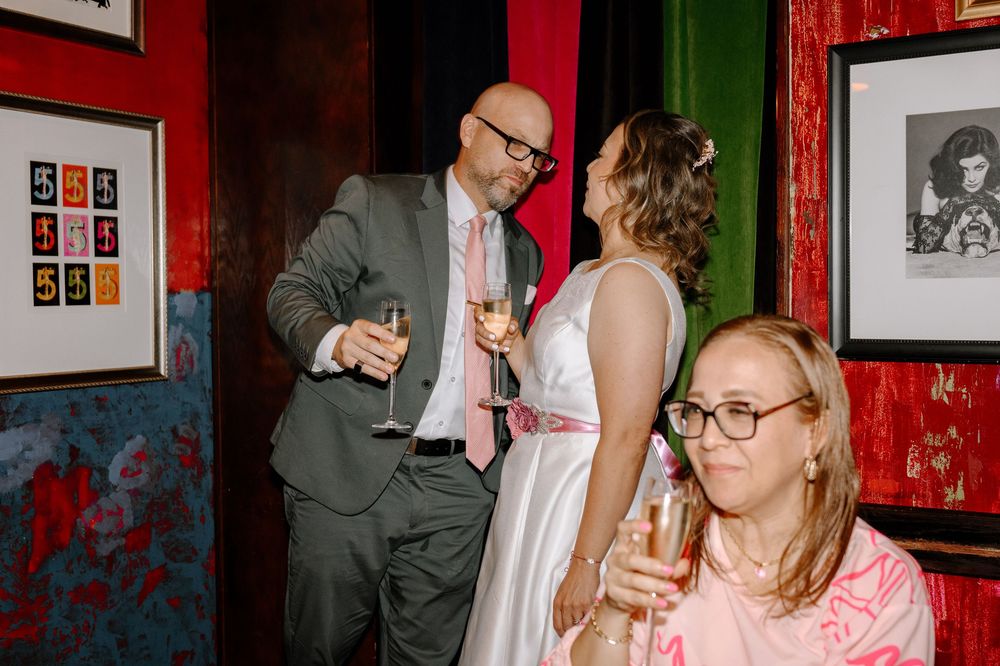 People enjoying drinks and socializing at a bar or party venue with red walls and framed artwork in the background.