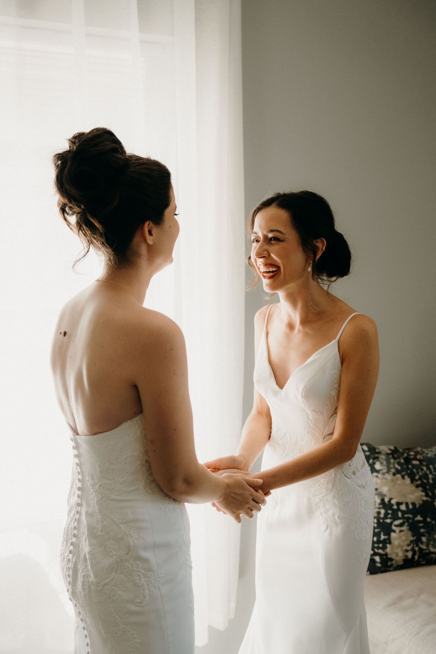 Two women in white wedding dresses share a joyful moment together as they prepare for their special day. The Sanctuary Roosevelt Island