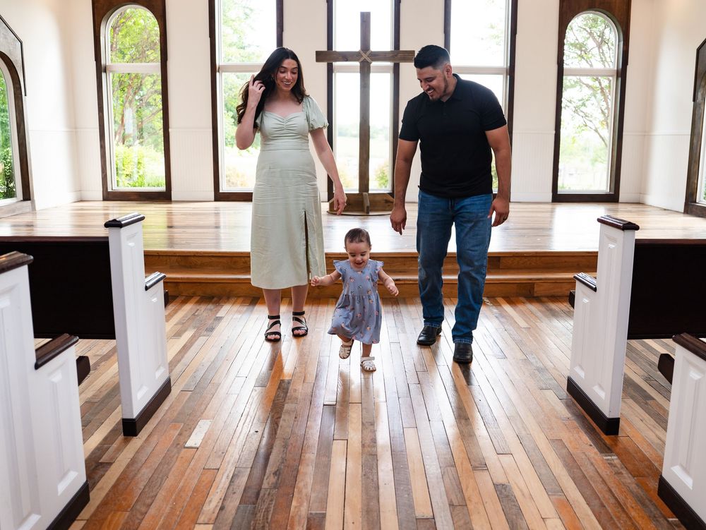 People visit an art gallery with polished wood floors and white columns, viewing artwork displayed along the walls.