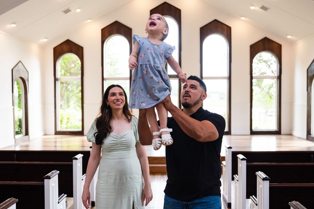 Wedding party poses in an elegant white church during a celebration with natural light streaming through arched windows.