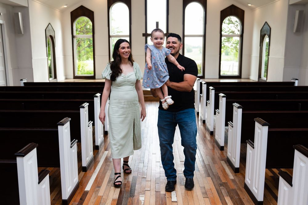 Couple walking down a church aisle holding hands in a casual pose with wooden pews on both sides.