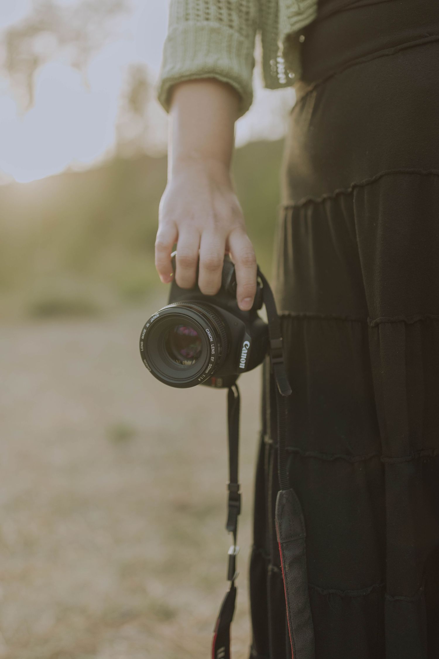 Canon camera being held by person in long black skirt and green cardigan.