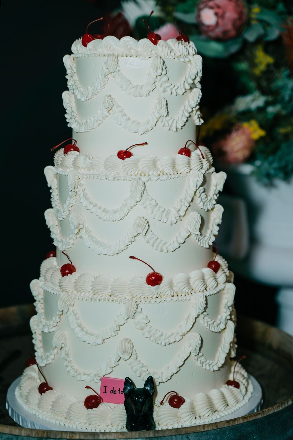 A multi-tiered white wedding cake decorated with delicate piping and red cherries as accents.