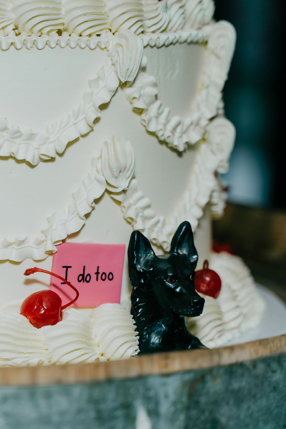 Wedding cake detail showing black scottie dog decorations and red cherries with text saying 'I do too' on pink label.