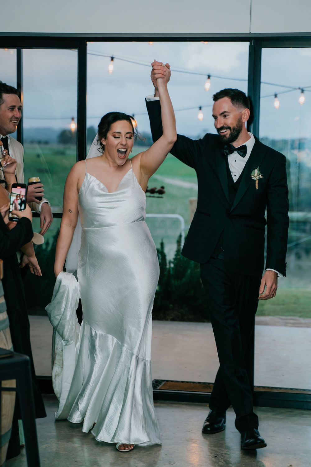 Newlyweds celebrating and dancing together at their wedding reception with string lights in the background.
