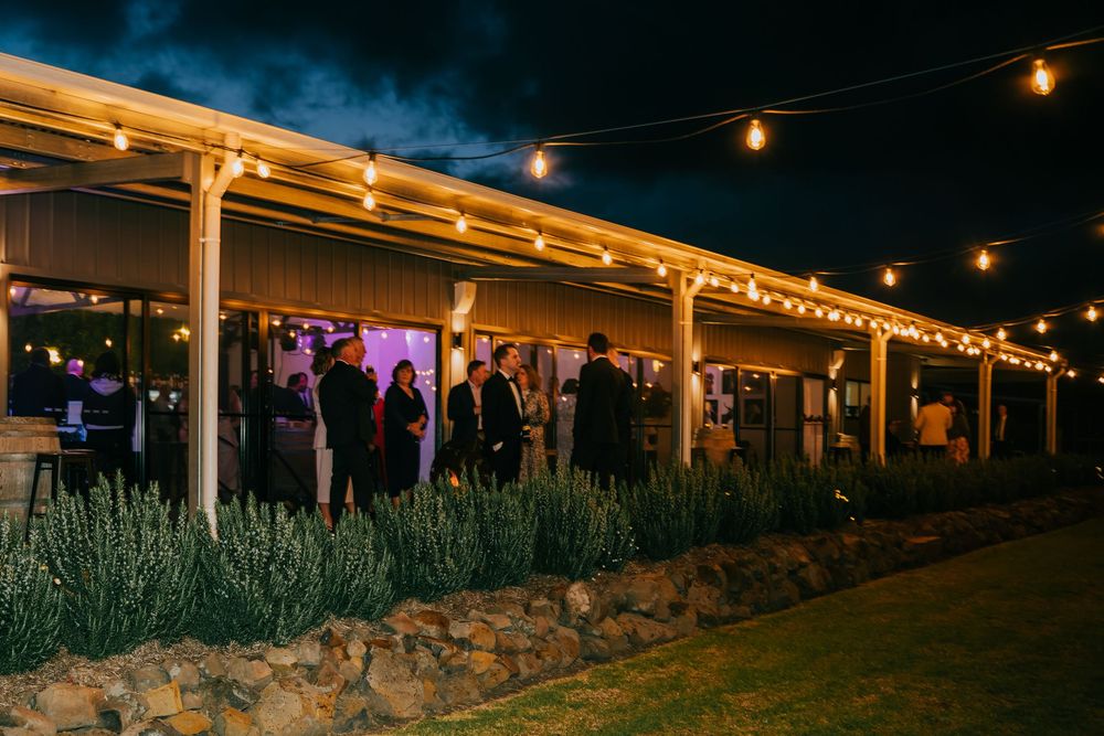 String lights illuminate a rustic outdoor patio with stone landscaping and wooden overhangs at dusk.