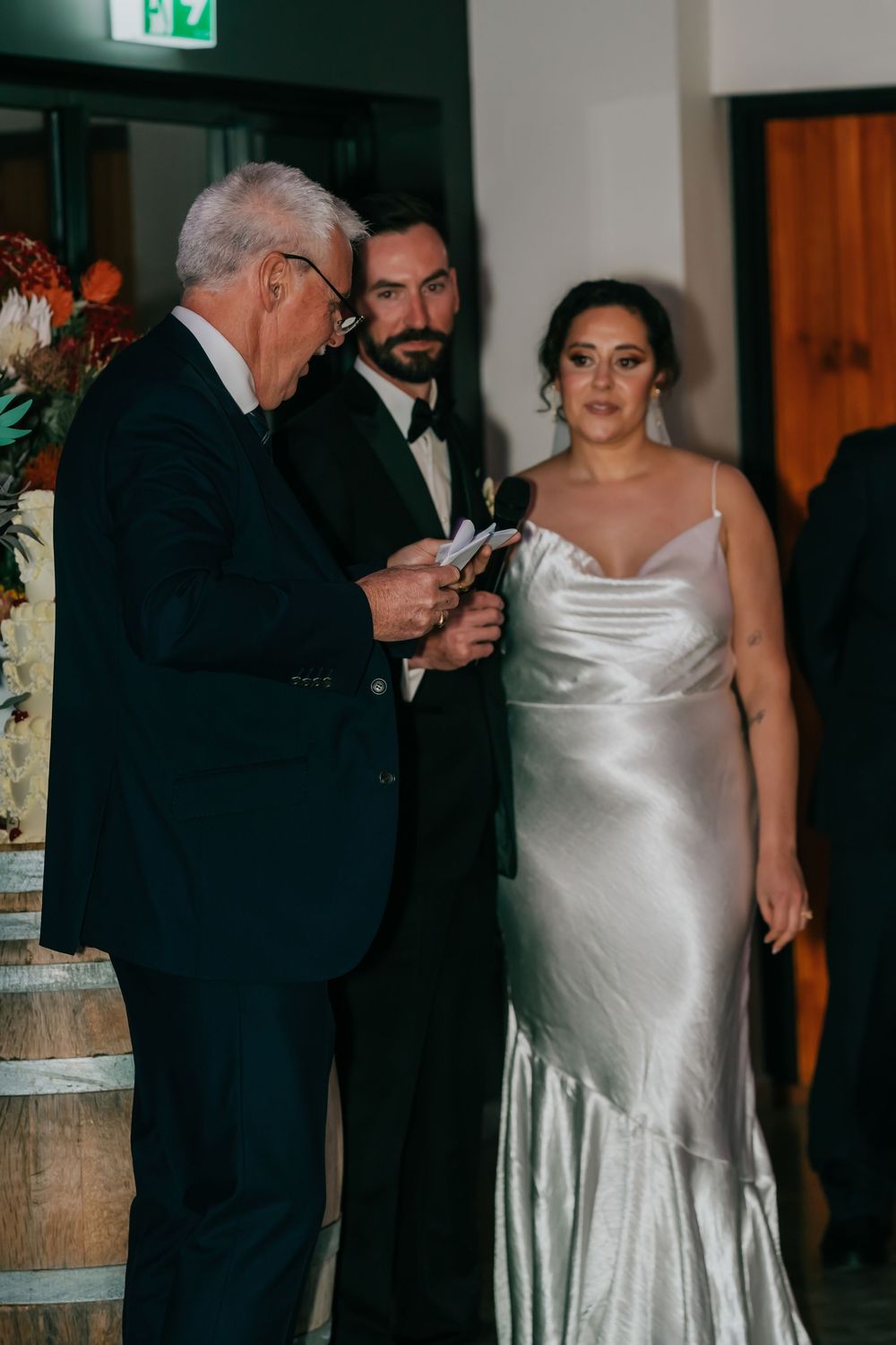 A bride in a sleek white satin gown dances with a partner at an intimate indoor wedding reception.