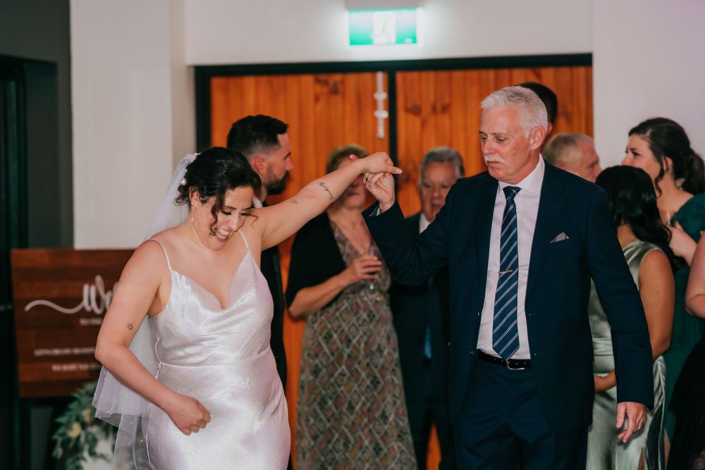 People dancing and celebrating at a dimly lit indoor wedding reception venue at night.