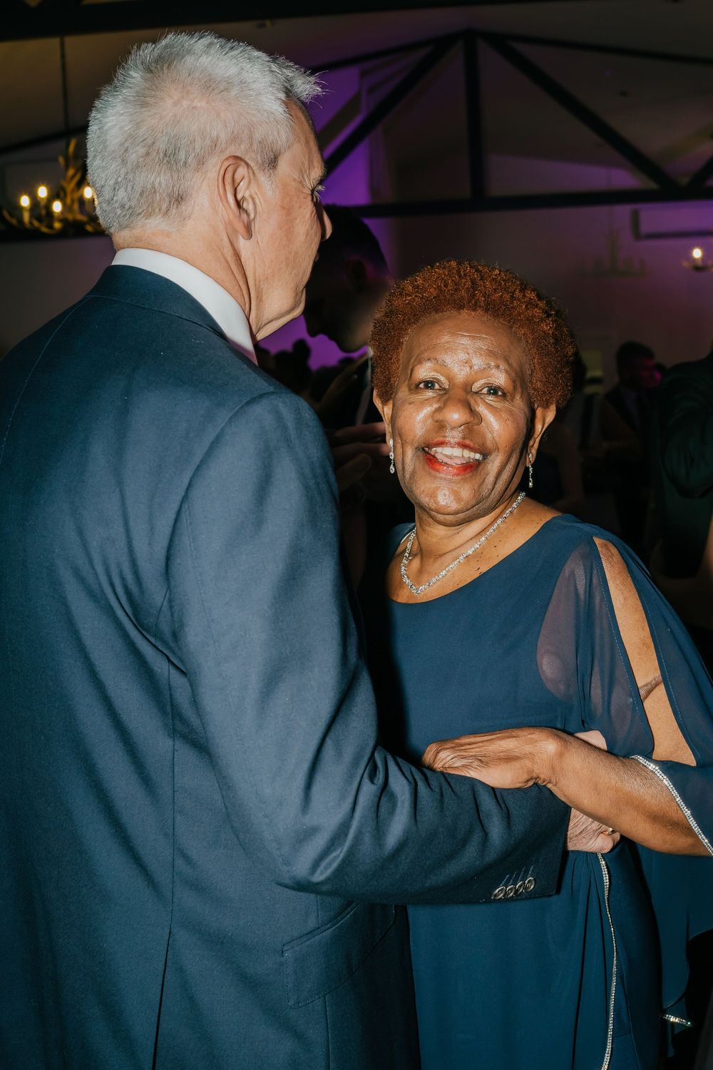 Couple dancing together at an elegant evening event with purple mood lighting in the background.