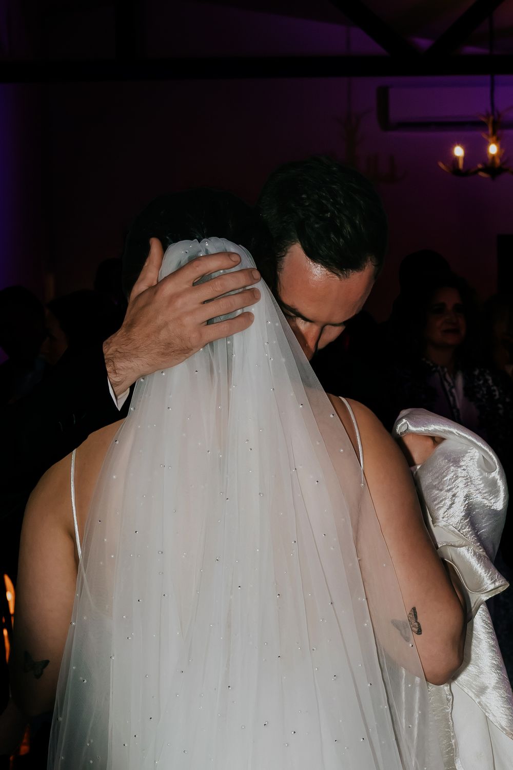 A couple in formal wedding attire dances together during their reception, with the bride wearing a flowing veil.