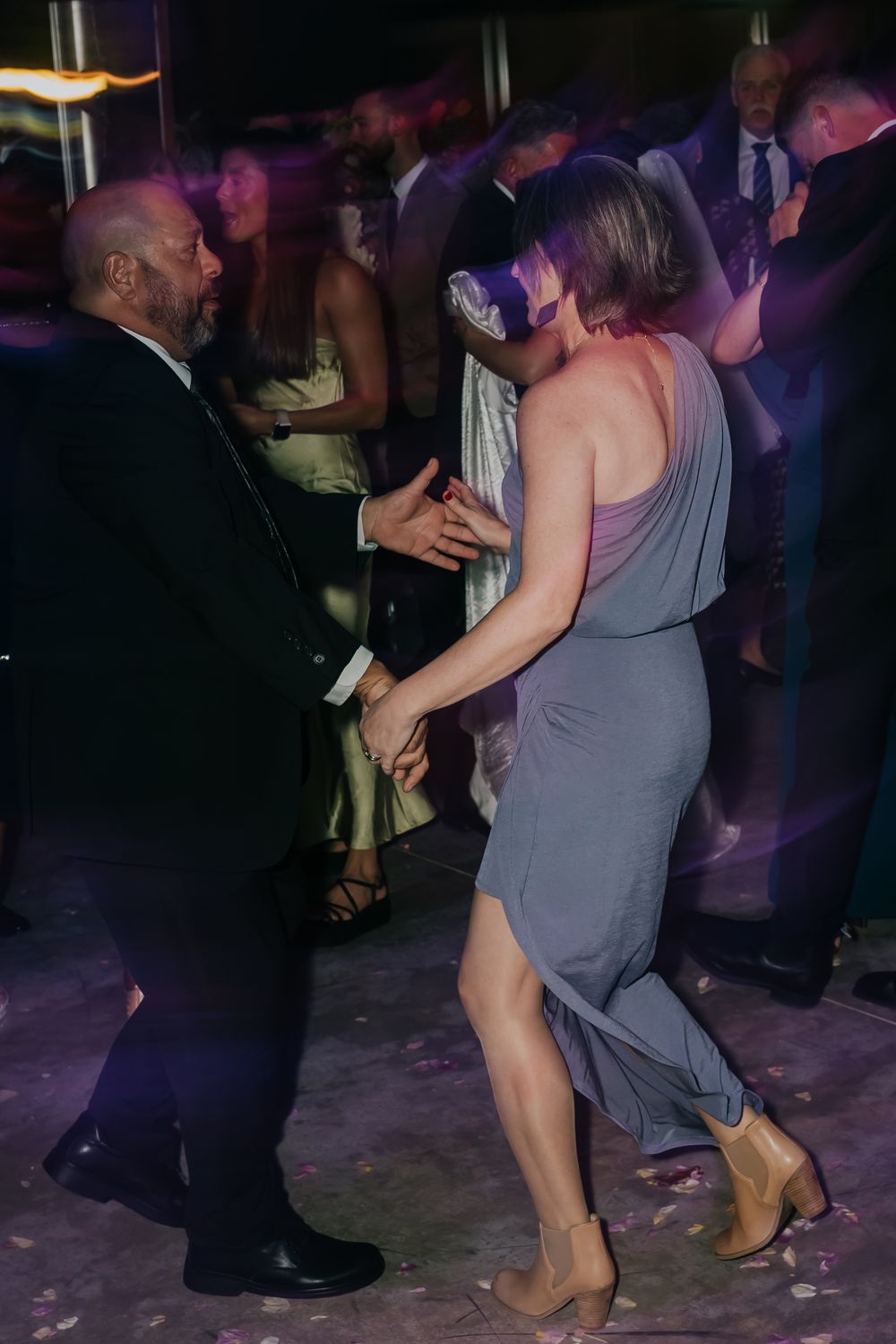 People dancing together at a dimly lit party or reception with purple lighting and festive atmosphere.